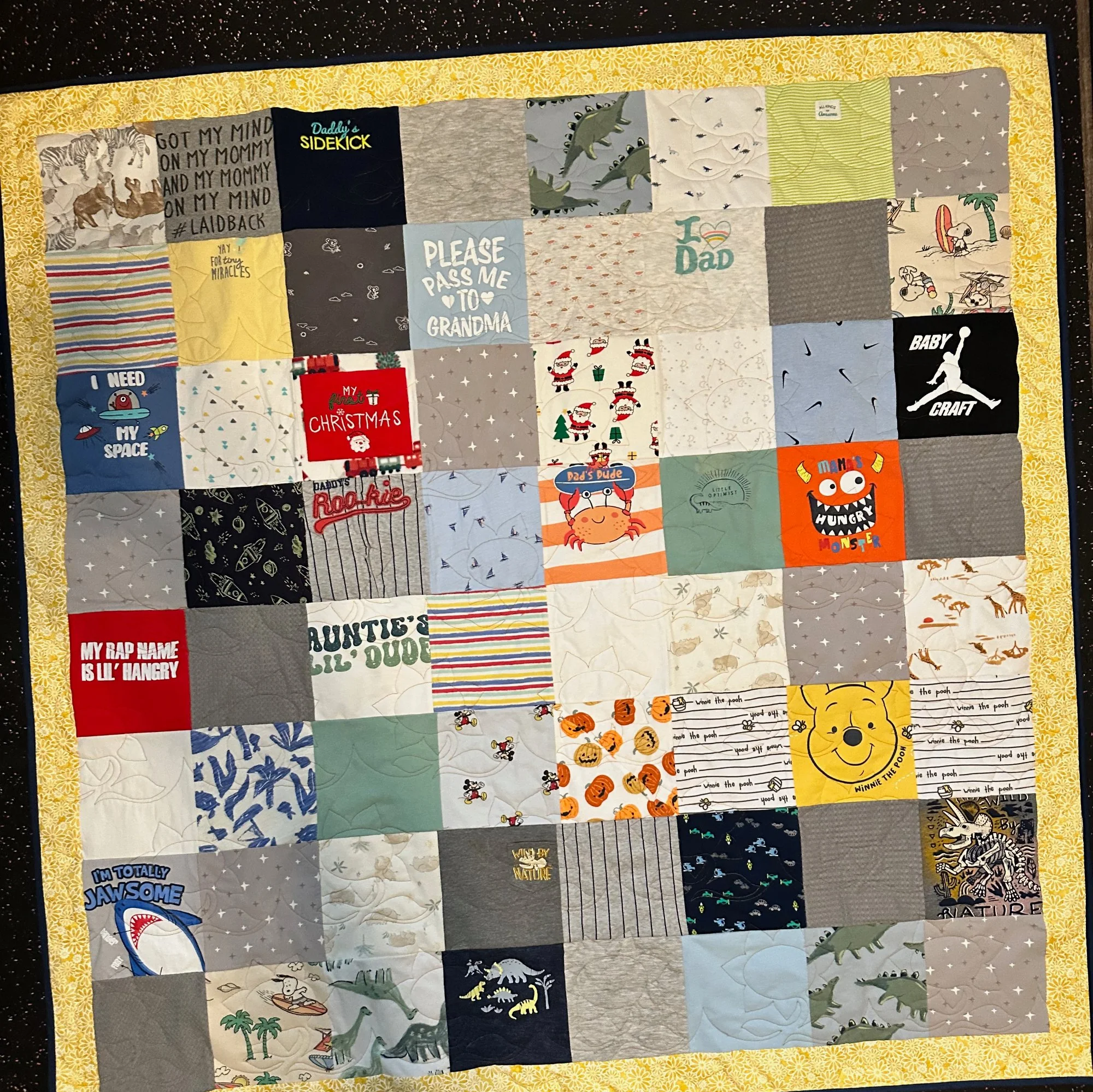 A memory quilt made from baby and toddler t-shirts and onesies with a yellow floral border, handmade in Atlanta by Quilts by Big Wes