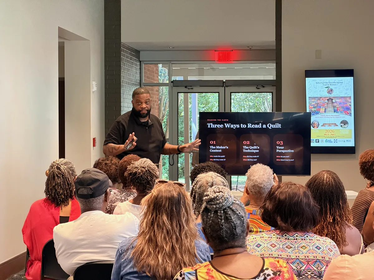 Wesley Hall speaking at the Atlanta Quilt Festival with a projected image of a nineteenth century narrative quilt behind him