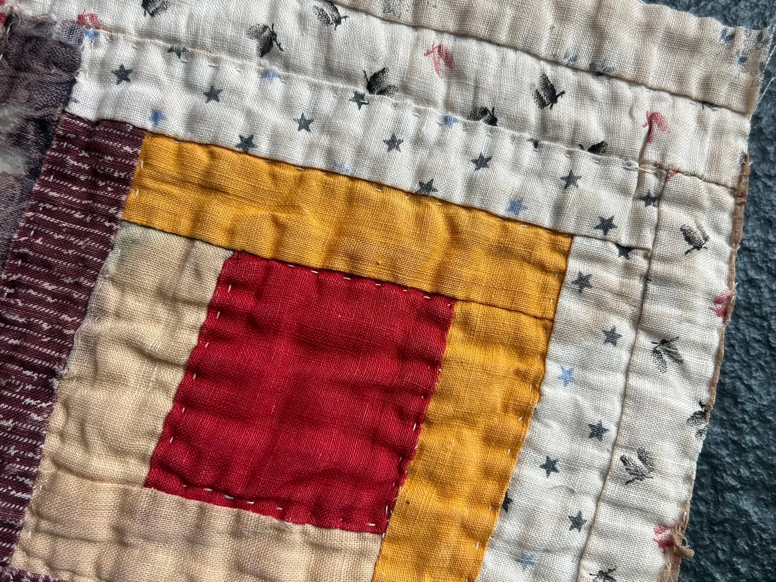 Close view of a vintage Log Cabin quilt block showing the center square with light strips on two sides and dark strips on the other two, forming a diagonal split