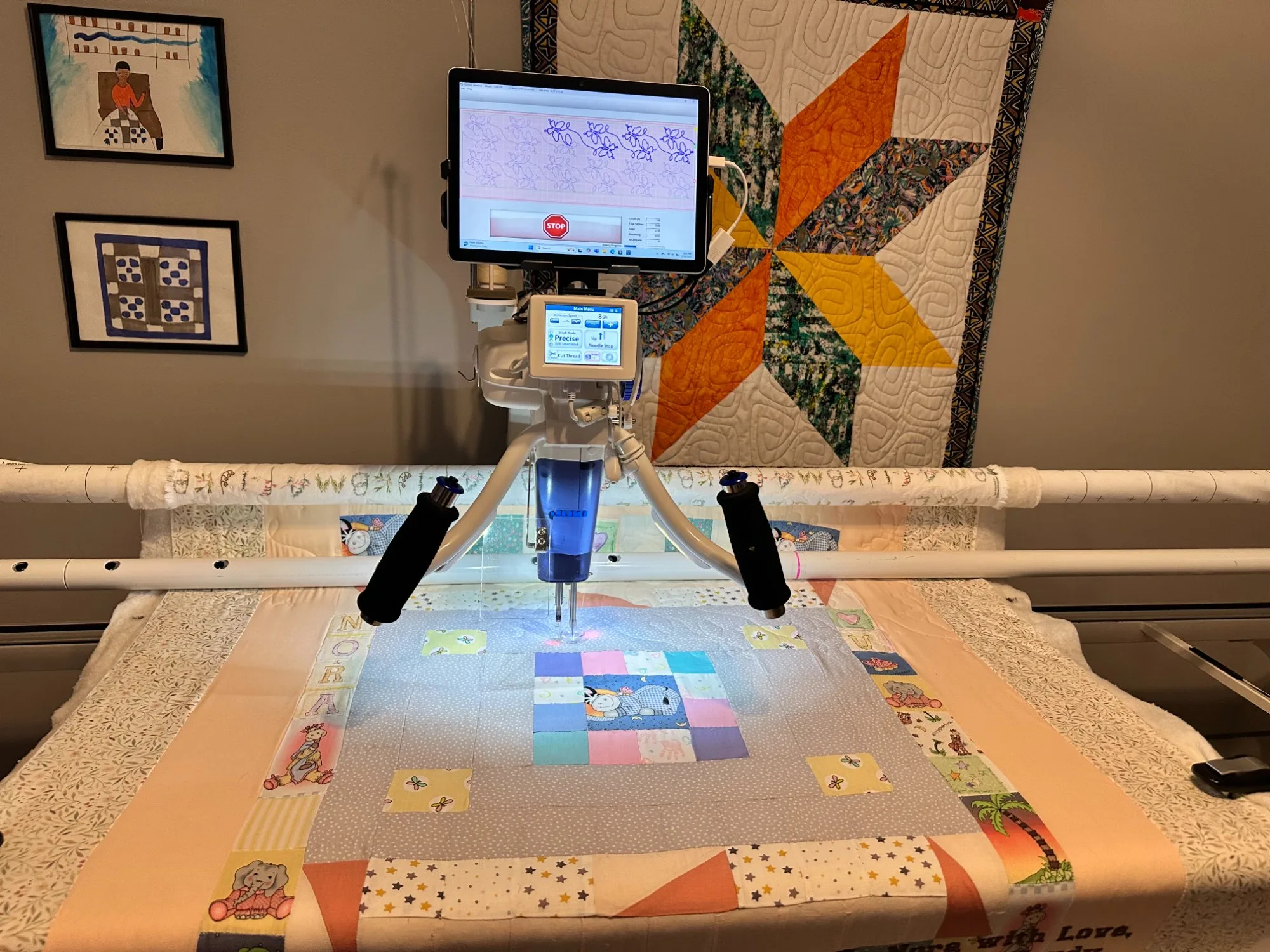 Computerized long arm quilting machine stitching a custom pattern on a baby quilt with pastel alphabet border fabric