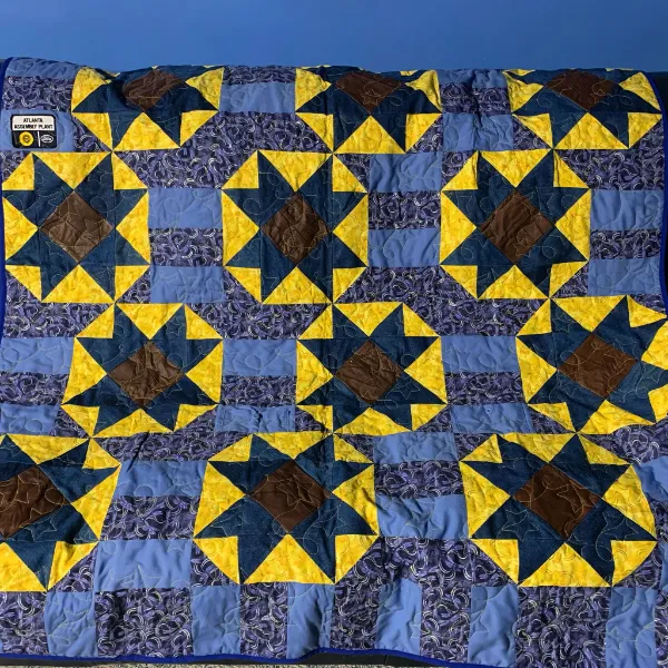 Custom star and pinwheel pattern quilt in navy, gold, and brown with an Atlanta Assembly Plant commemorative patch, longarmed by Quilts by Big Wes