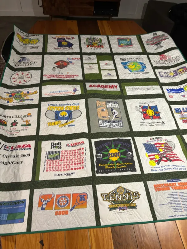 Large tennis career t-shirt quilt with dark green sashing displayed overhead on a table, featuring over 30 USTA Southern Section tournament shirts, handmade in Atlanta
