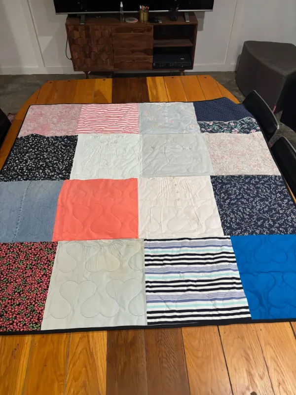 Memory quilt made from a woman's clothing collection including floral blouses, striped shirts, denim, and patterned fabrics, displayed flat in Atlanta