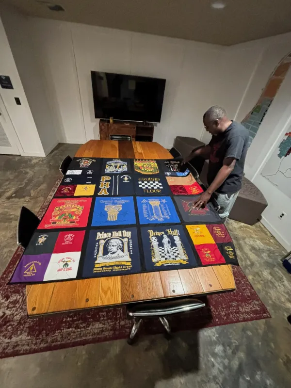 Client reviewing his Prince Hall Masonic t-shirt quilt displayed on a table at the Quilts by Big Wes studio, featuring Shrine and Masonic chapter shirts