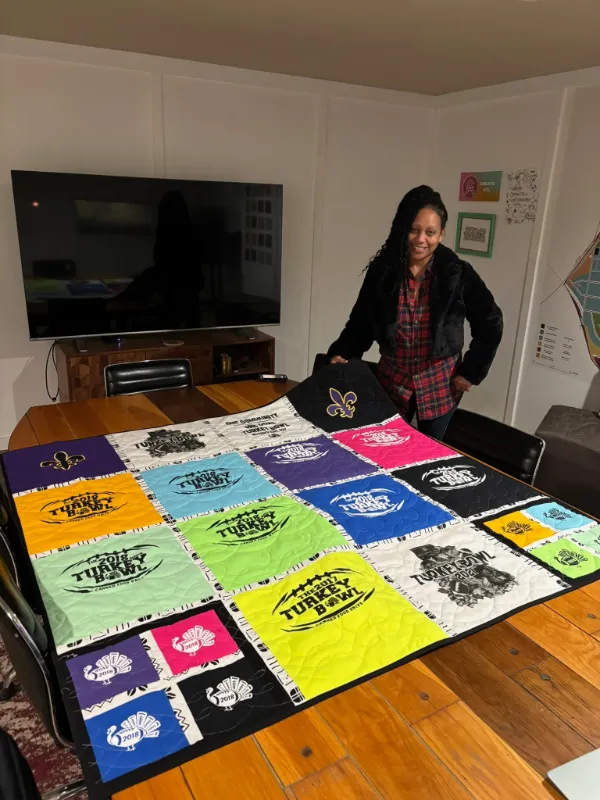 Client displaying a vibrant multi-colored Turkey Bowl charity t-shirt quilt at CreateATL in Atlanta, made by Quilts by Big Wes
