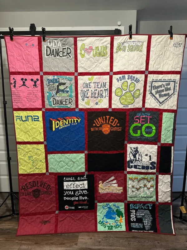 Cheerleading, school, and faith t-shirt quilt hung on a display rack, featuring UDA Dancer, Pom Squad, and church event shirts, handmade in Atlanta