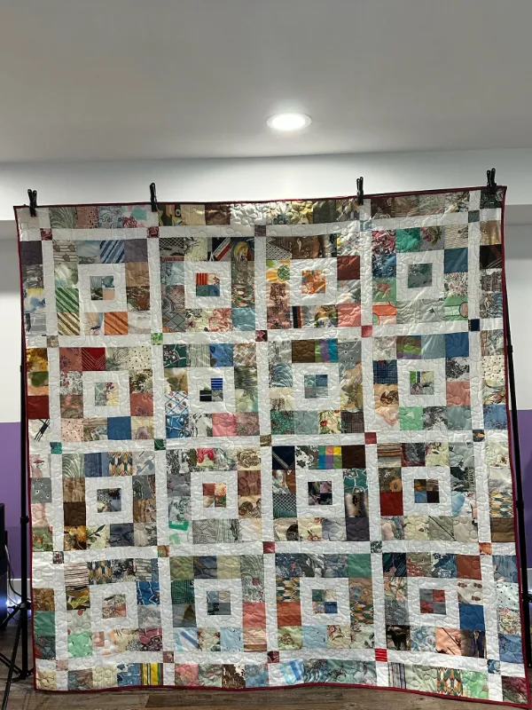 Large scrappy log cabin memory quilt made from hundreds of fabric pieces in every color, hung on a display rack at the Quilts by Big Wes studio in Atlanta