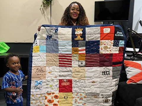 A woman holding the custom t-shirt quilt made for her son by Quilts by Big Wes