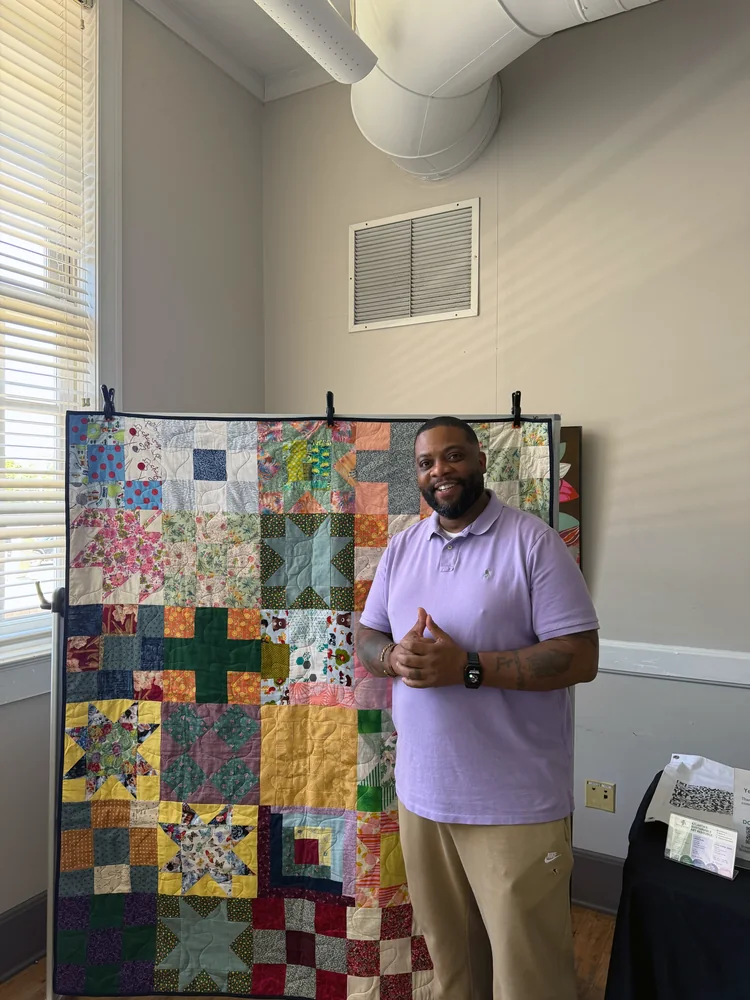 Wesley Hall standing in front of a sampler quilt