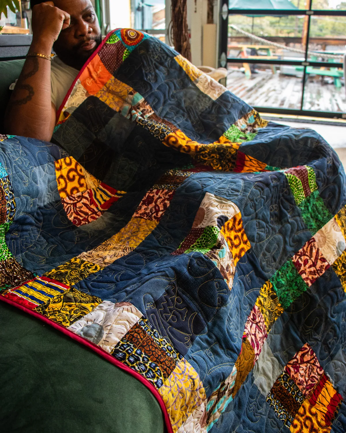 Wesley Hall in a thoughtful pose alongside a custom art quilt pieced from African wax prints, kente cloth, and denim panels
