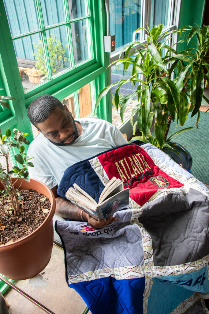 A man reading a book wrapped in a t-shirt quilt